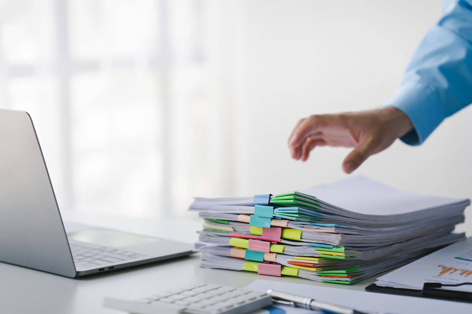 A laptop with stacks of sticky-tabbed paperwork — the messy inputs GRABBER processes.